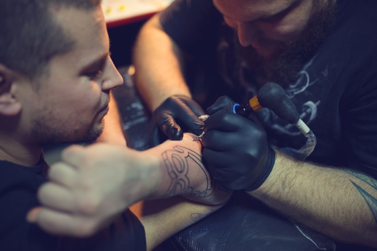 Tattoo artist tattooing mans forearm